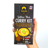 Hand holding a Siam Yellow Thai Curry Kit packaging on a white background
