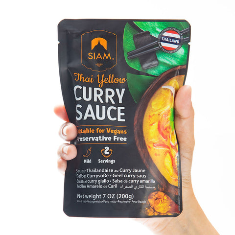 Hand holding a package of Siam Thai Yellow Curry Sauce on a white background